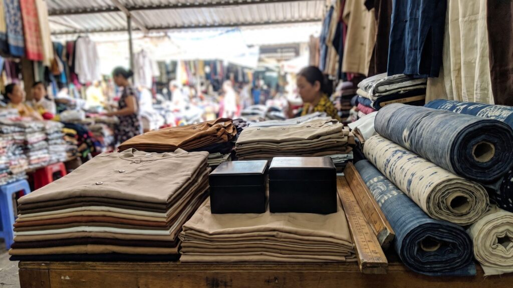 Folded shirts, plain black lacquer boxes and rolls of indigo ikat fabric on a stall table inside a covered market in Ho Chi Minh City
