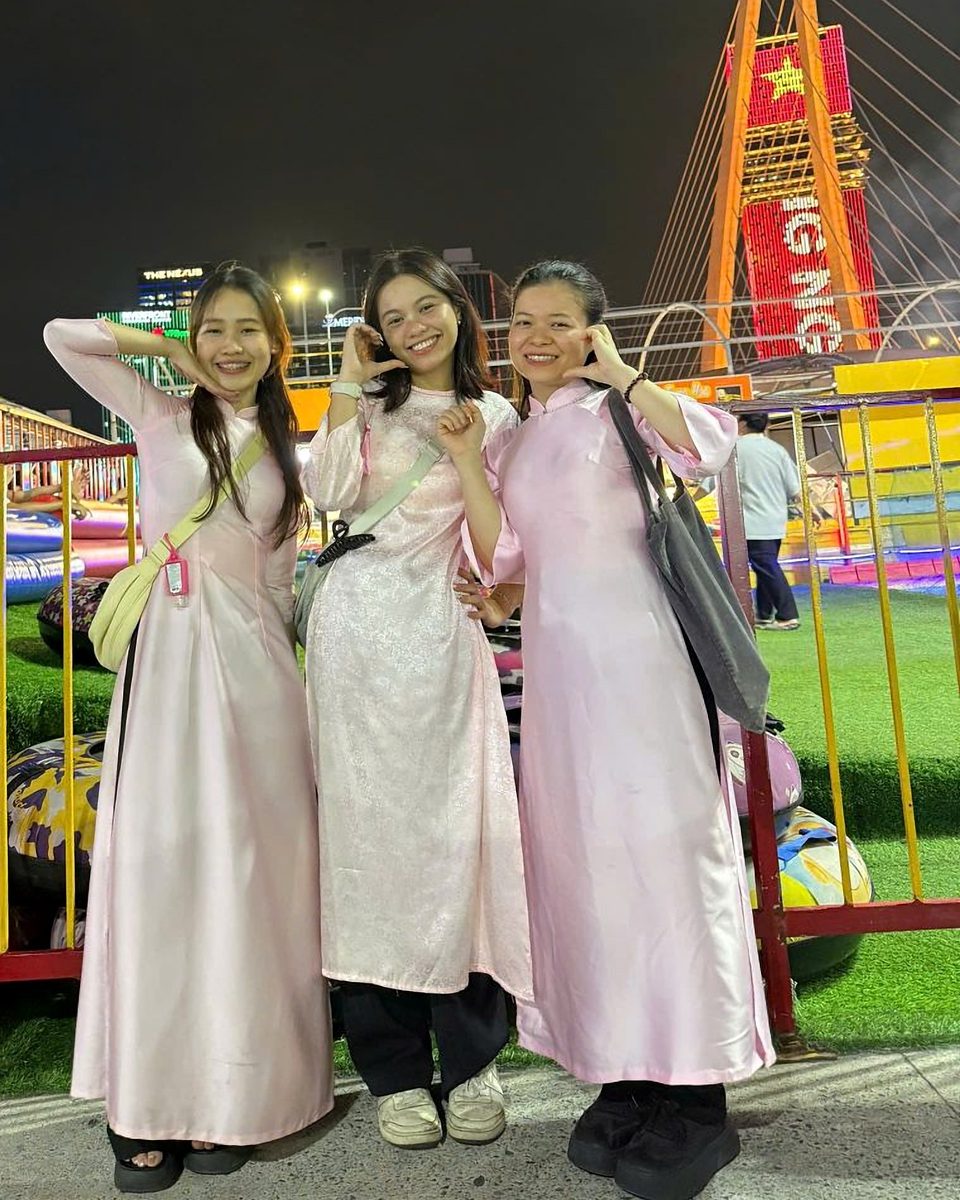 Three Miss Saigon Tours guides in pink ao dai at night near the Ba Son Bridge