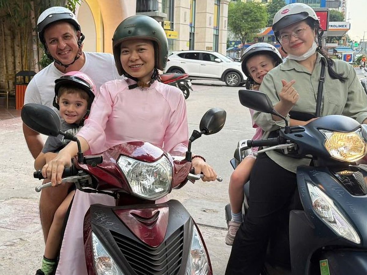 Two children in helmets riding with their parents and Miss Saigon Tours guides on scooters in Ho Chi Minh City